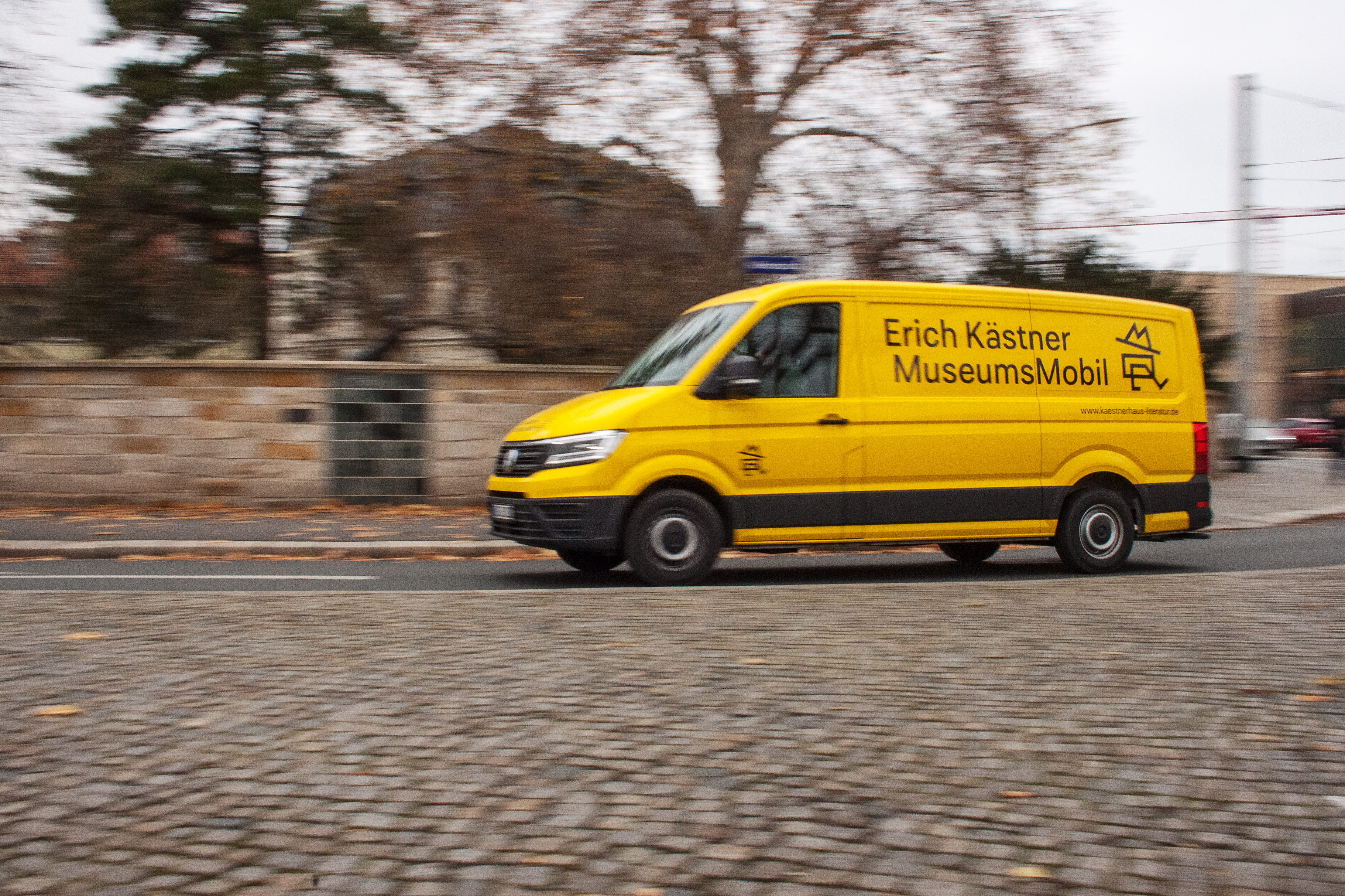 Ein gelber Klein-Bus mit der Aufschrift Erich Kästner MuseumsMobil fährt auf der Straße vorbei.