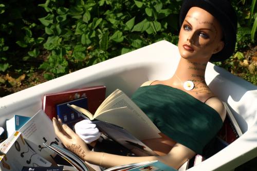 Lesende Puppe in einer Badewanne voller Bücher